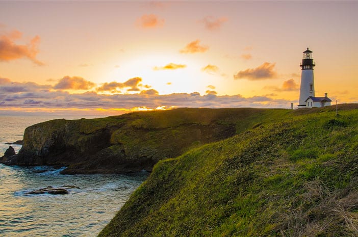 Lighthouse near ocean at sunset.